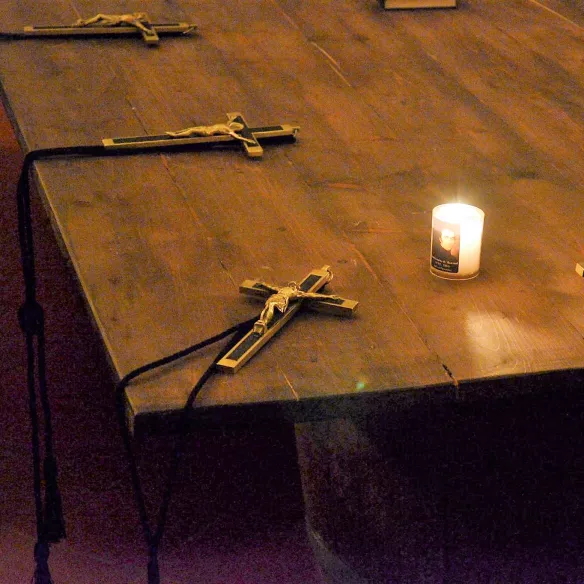 Kreuze, die auf einem Tisch um eine Kerze gruppiert liegen.